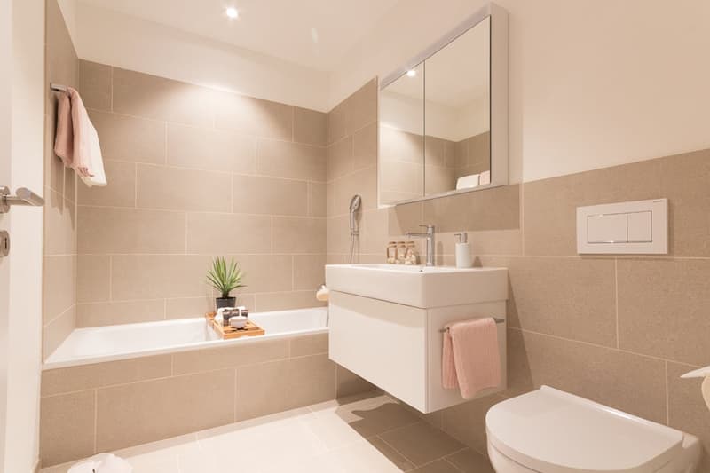 Bathtub, sink, shower, toilet, white tiles, mirror, pink towels, plant, modern design
