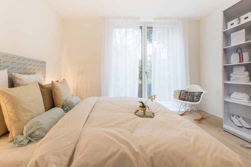 large bed, pillows, bedside tray, sliding glass door, white curtains, white shelves, chair