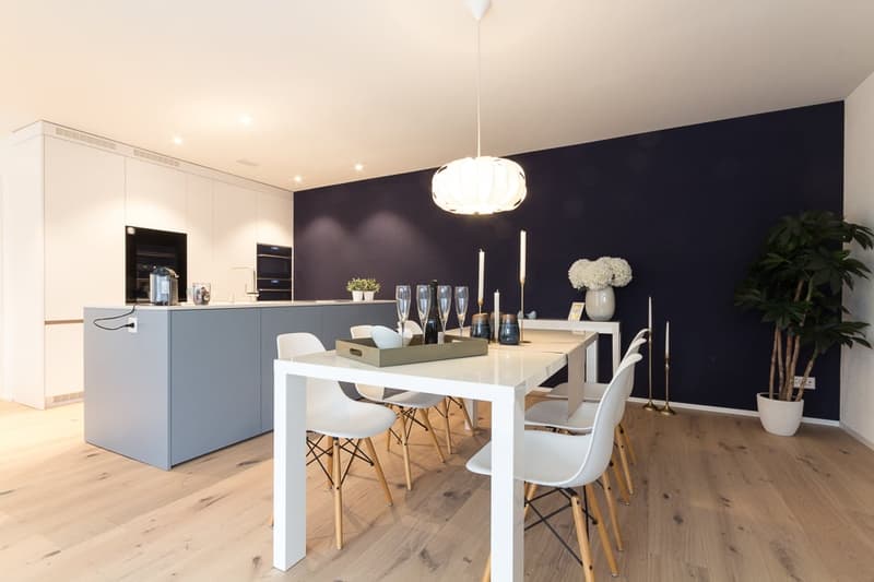 modern dining area with wooden floor, blue wall, white kitchen island, white dining table with chairs, pendant light, plants, candles, wine glasses