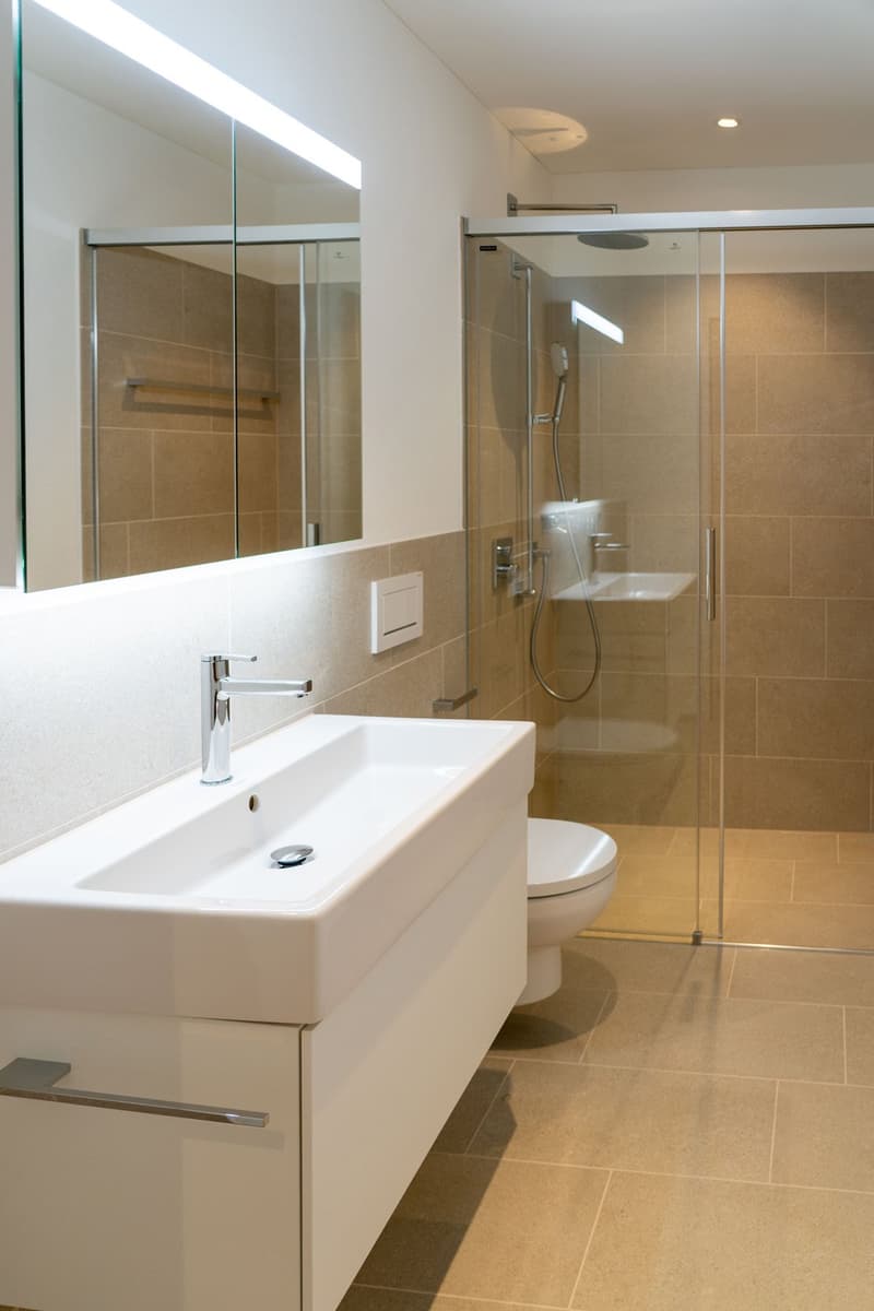 modern bathroom with white sink, white toilet, glass shower enclosure, mirror, beige tiles