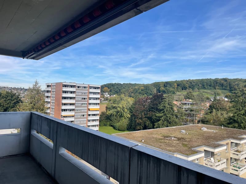 balcony with railings, view of a building, trees, and hills