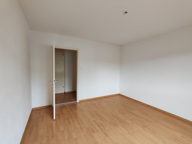 empty room with wooden floors, white walls, an open door leading to another room