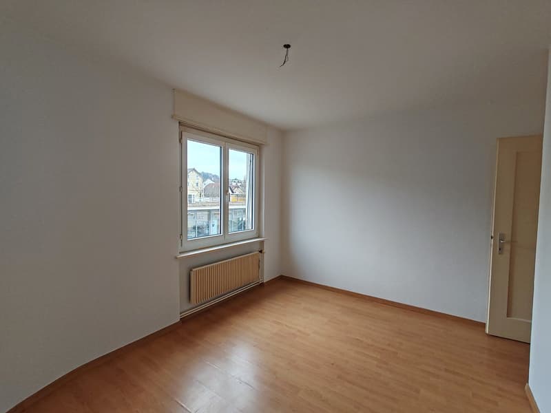 Empty room with white walls, wooden floor, a window, and a radiator