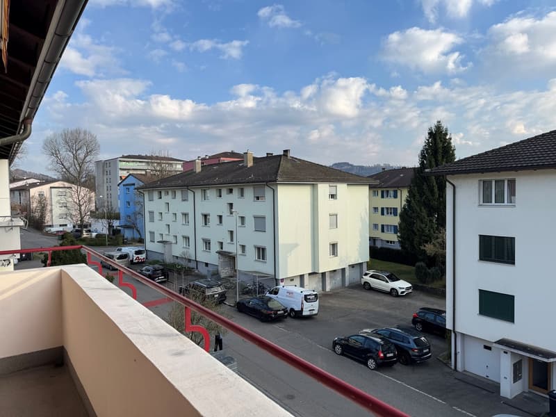 A balcony with a view of a street with several cars parked in front of a building.