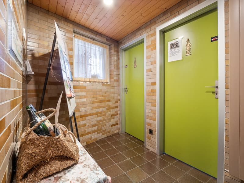 Brick walls, wooden ceiling, tiled floor, artwork on the wall, a basket with items, and a green door leading to another room