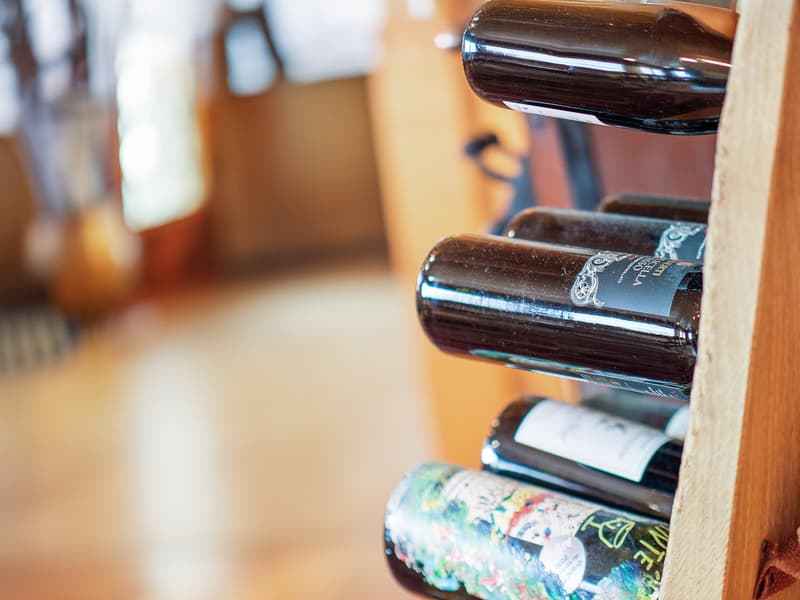 Wooden wine rack holding several bottles of wine, including a bottle with a label that appears to be a dishwasher brand or logo.