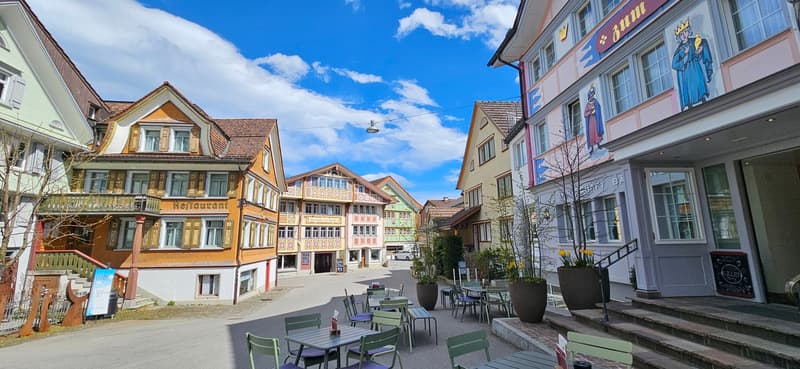 Charming historic town with colorful, traditional-style buildings, outdoor seating area, and a blue sky with clouds overhead.