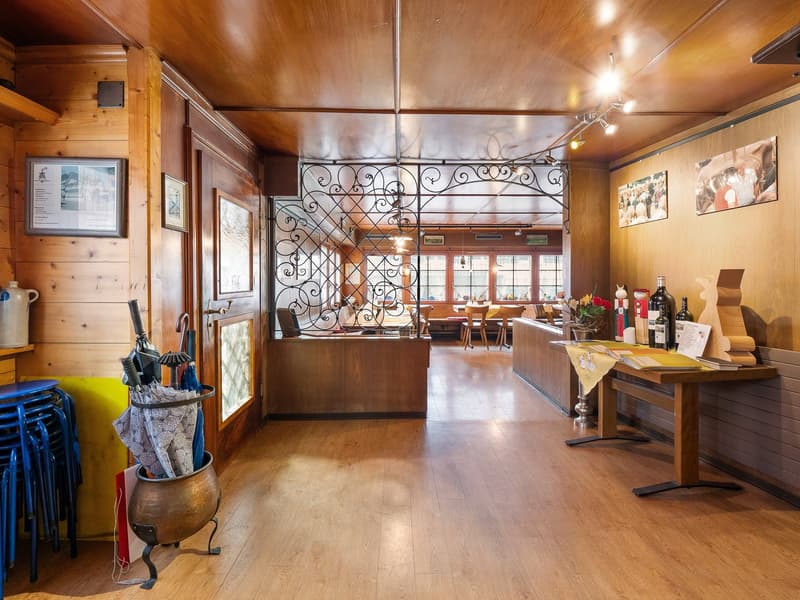 The image shows a cozy, rustic-style interior of what appears to be a restaurant or cafe. The space features wooden walls and ceilings, with a wrought-iron decorative partition separating the dining area from the rest of the space. There are framed artwor