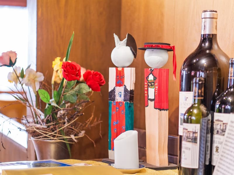 The image shows a cozy interior with a wooden wall, a bouquet of red roses, and decorative figurines. There are also several wine bottles visible, suggesting this may be a dining or living room area.