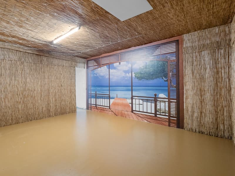 Empty room with light brown floor, bamboo walls, and mural of a balcony with sea view