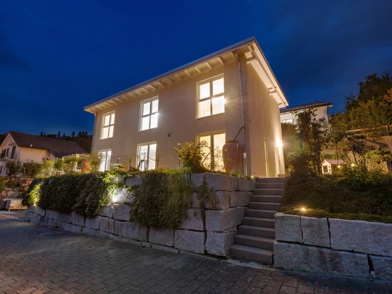 Modern 2 story house, beige exterior, many windows, steps, illuminated at night