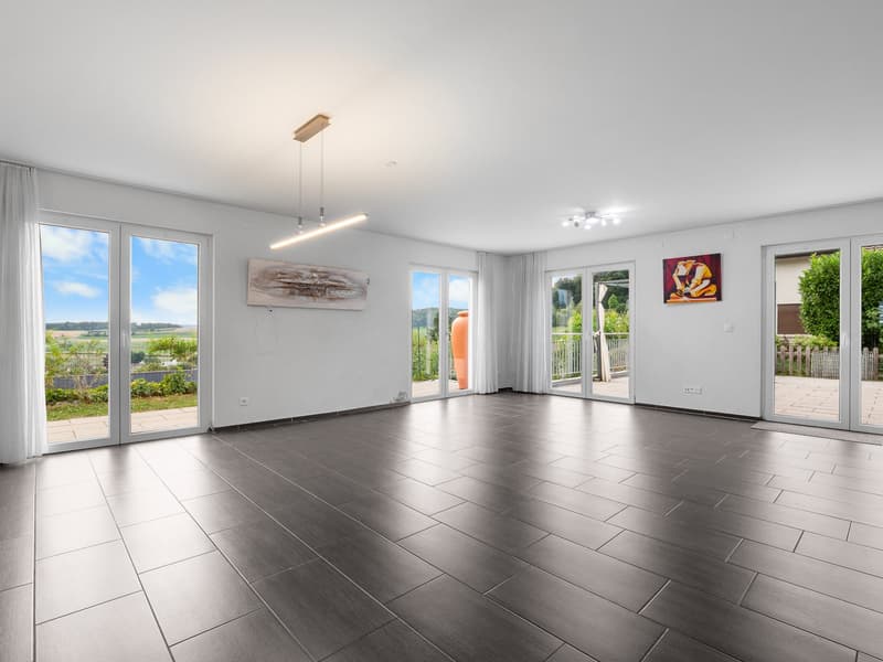 Empty room with large sliding doors leading to a balcony, white walls, ceiling lights, tiled floor, and two paintings.