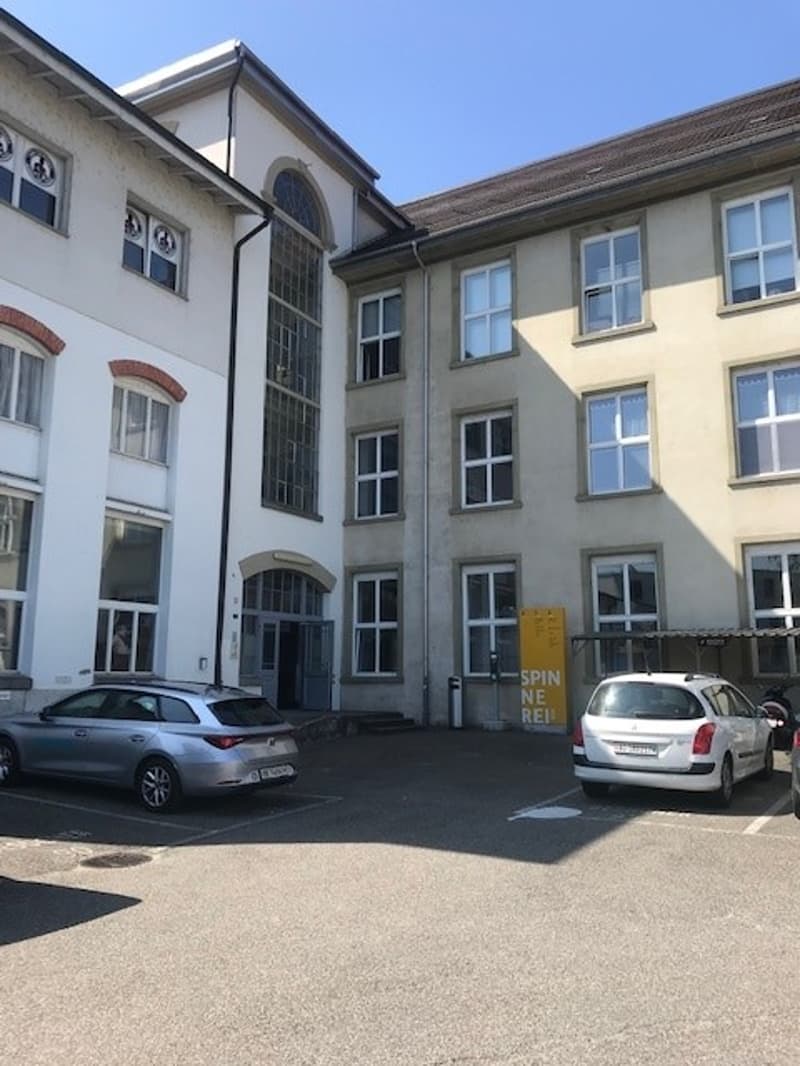 3-story building with white and yellow exterior, arched windows, and a parking area in front.