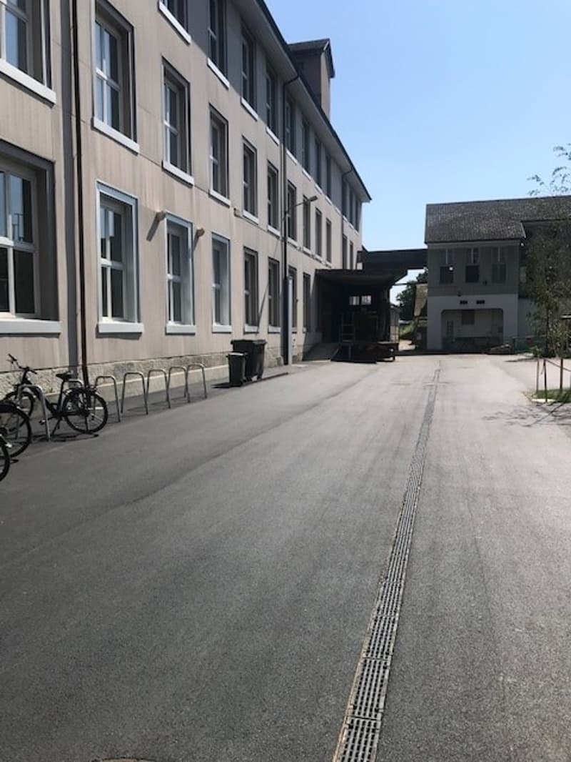 A multi-story building with a gray exterior, large windows, and a paved courtyard with bicycle racks.