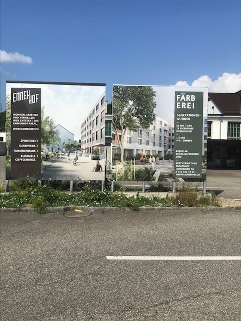 Two-story commercial building with signage for 'Endehof' and 'FarbErei', surrounded by trees and greenery, with people walking in the foreground