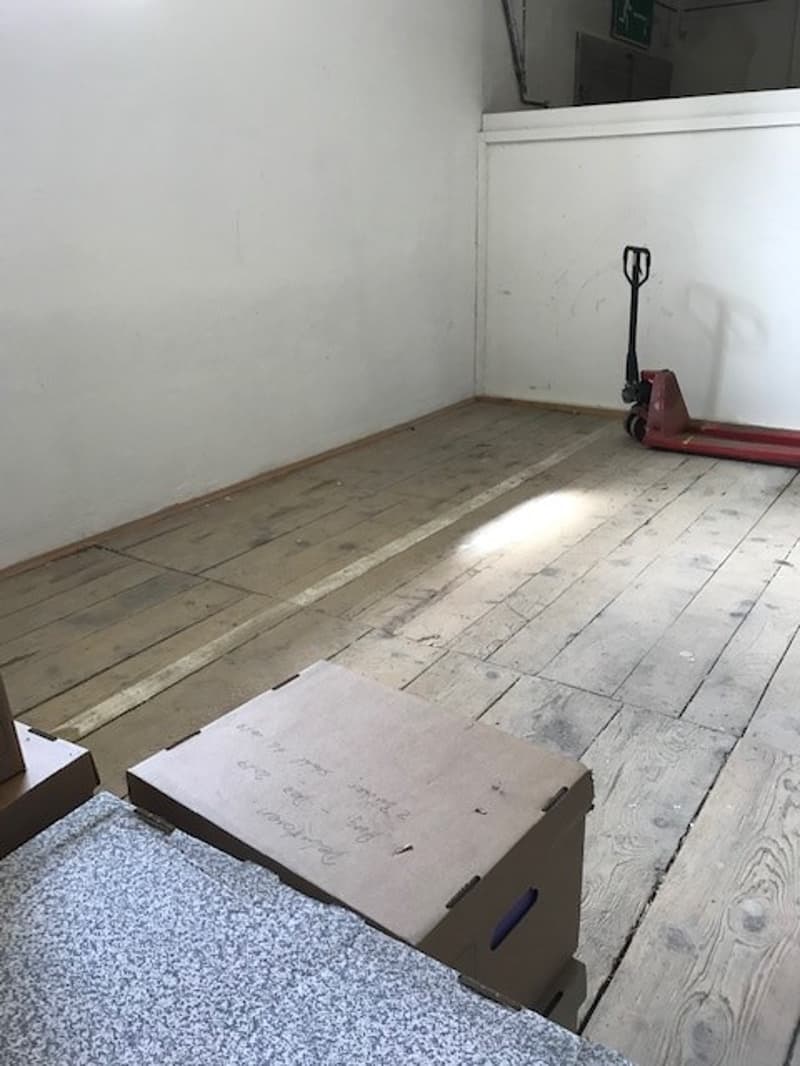 Empty room with concrete floor, white walls, and a red hand truck in the corner.