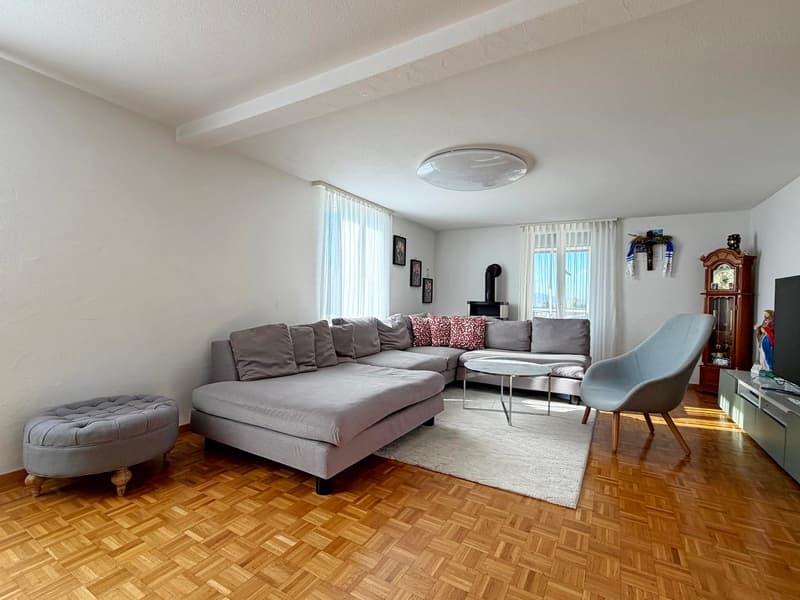 white walls, wooden floor, L-shaped sofa, round coffee table, armchair, rug, wooden grandfather clock, television, decorative items