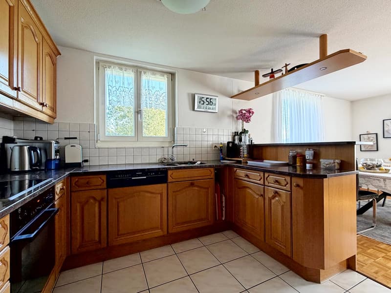 Modern kitchen with wooden cabinets, stainless steel appliances, granite countertop, dishwasher, washing machine, and a window with curtains.