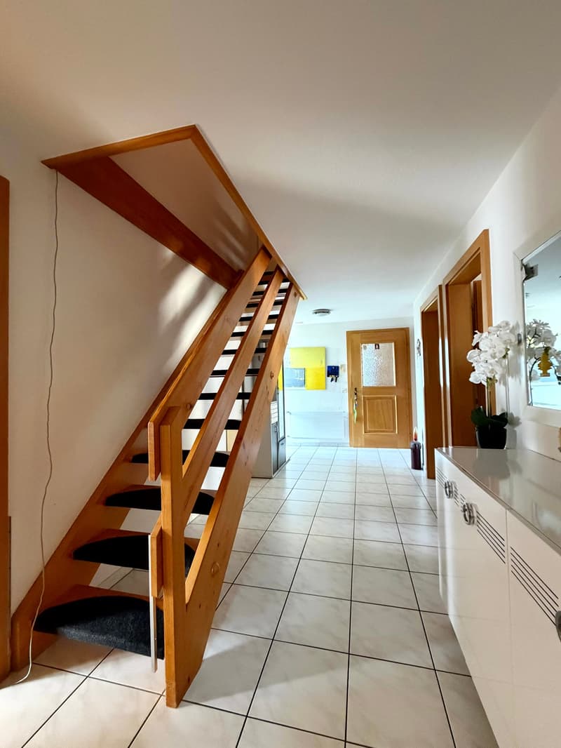 Staircase on the left, tiled floor, hallway, kitchen on the right, open door