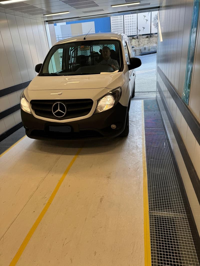 Mercedes van parked in a parking garage, yellow lines on the floor, white walls, metal grates on the side