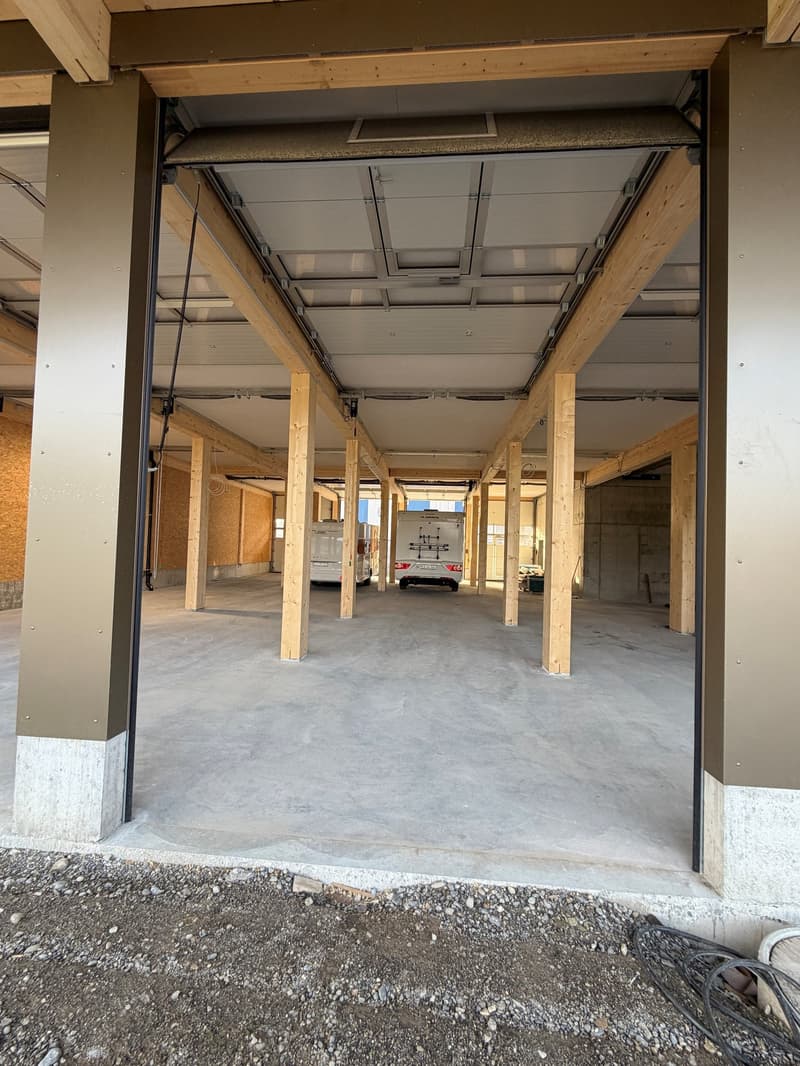 An open garage with wooden pillars, concrete floor, and two white vans parked inside.