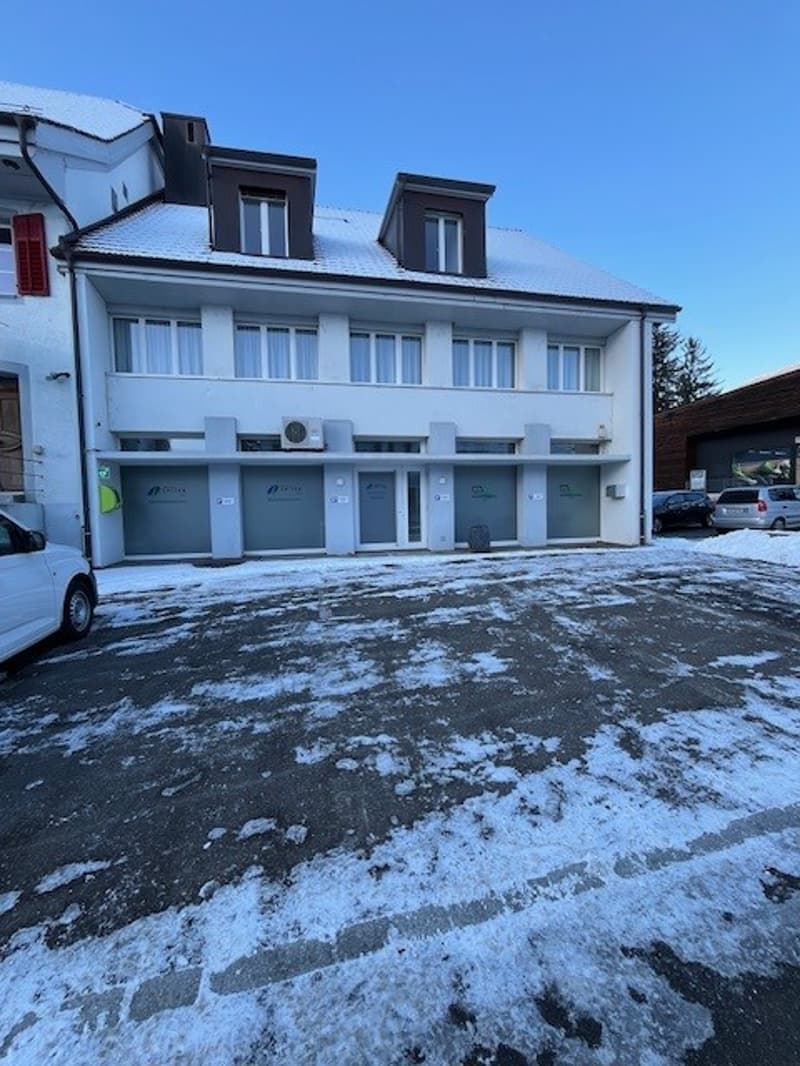 2 story white building, 5 garage doors, cars parked, snow on ground