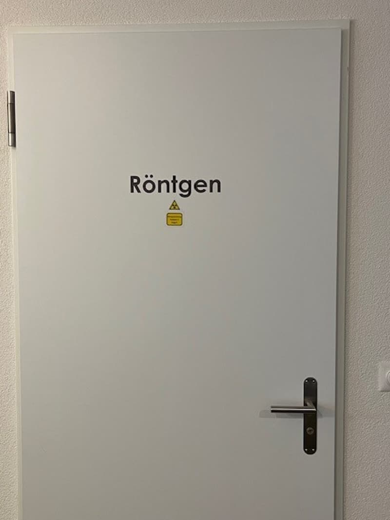 White door with silver handle and lock, word 'Rontgen' on the top, sign of radiation under the word