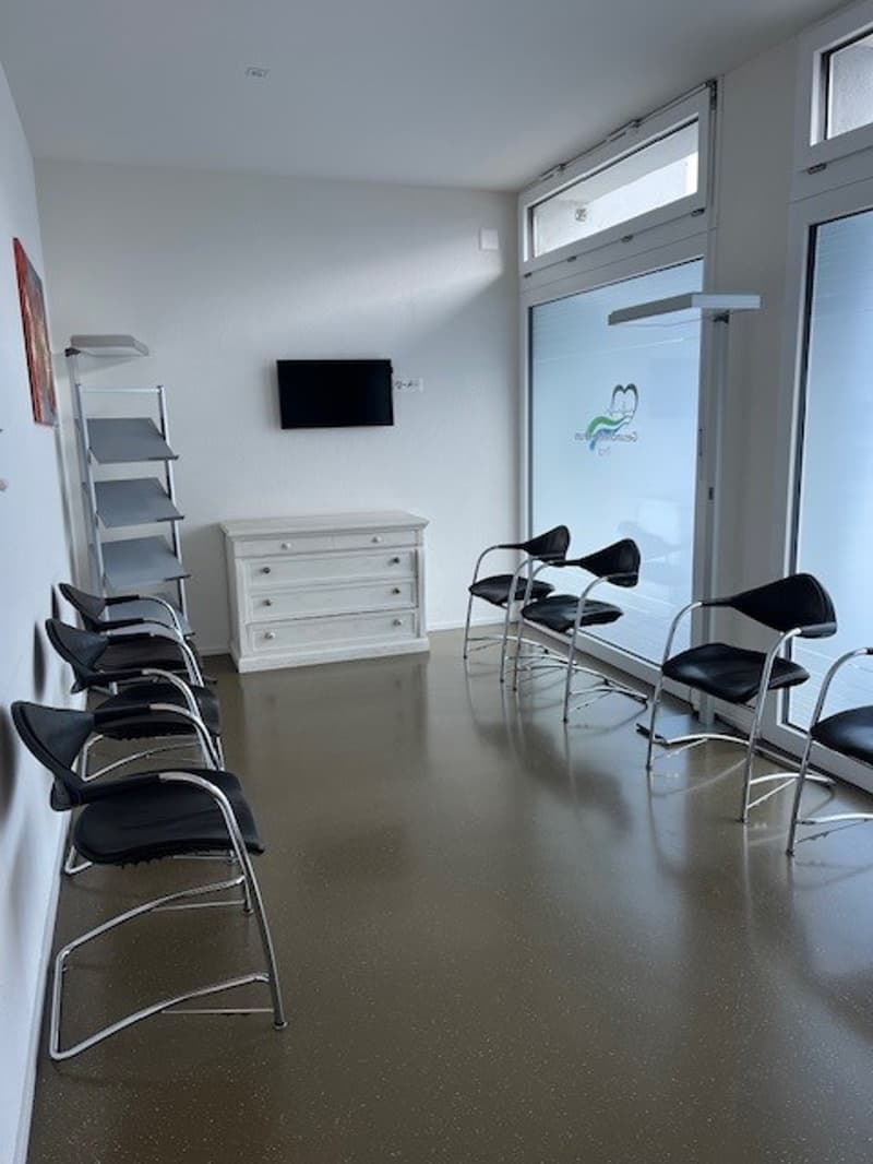 empty room with a television on the wall, a white dresser, and black chairs