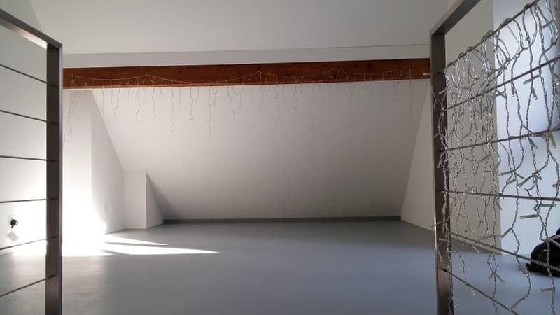 Empty room with white walls, wooden beams on the ceiling, and a large window with a metal grate covering it.