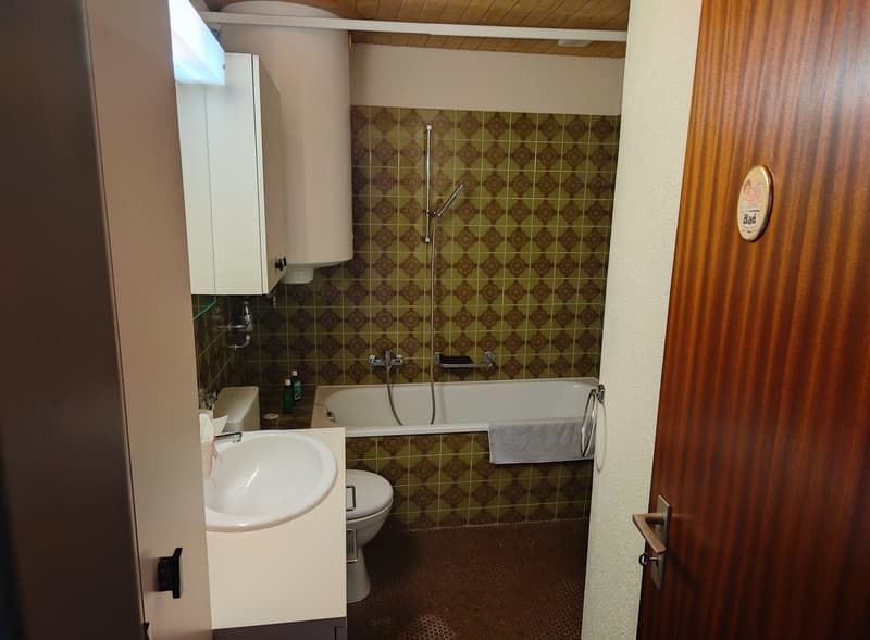 Bathroom with green tiles, a white sink, toilet, bathtub, a towel, and a shower