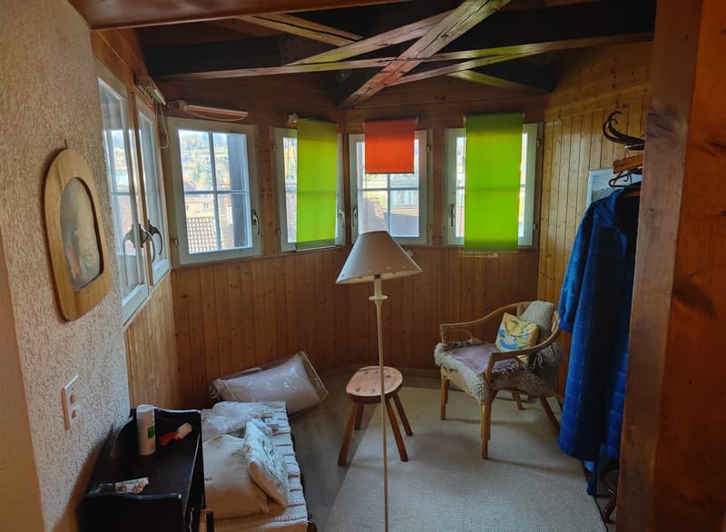 wooden wall, bed with pillows, chair with cushions, stool, lamp, picture frame, windows with blinds
