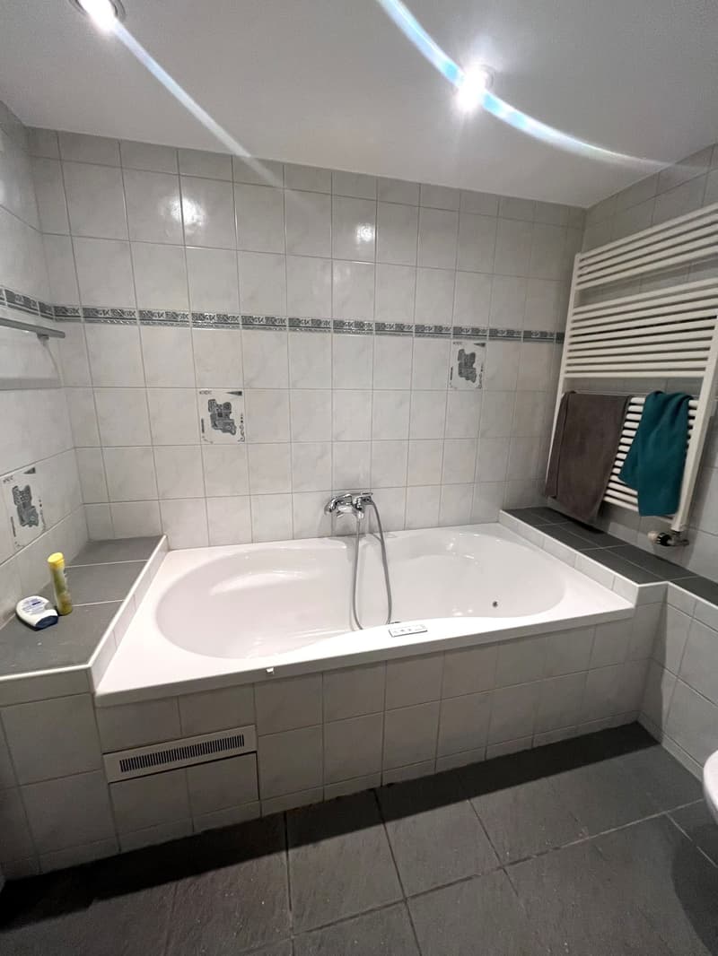 large white bathtub, white tiled walls, towel rack with towels, gray floor