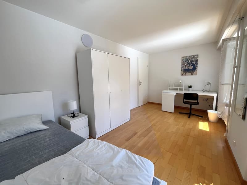 Single bed, nightstand, white lamp, white wardrobe, desk with black chair, desk lamp, picture frame, trash can, mirror, white walls, wooden floor