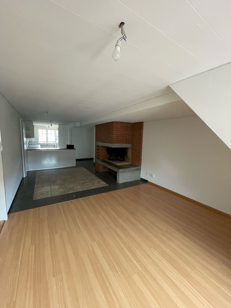Open-concept living room with hardwood flooring, a brick fireplace, and a kitchen area with tile flooring