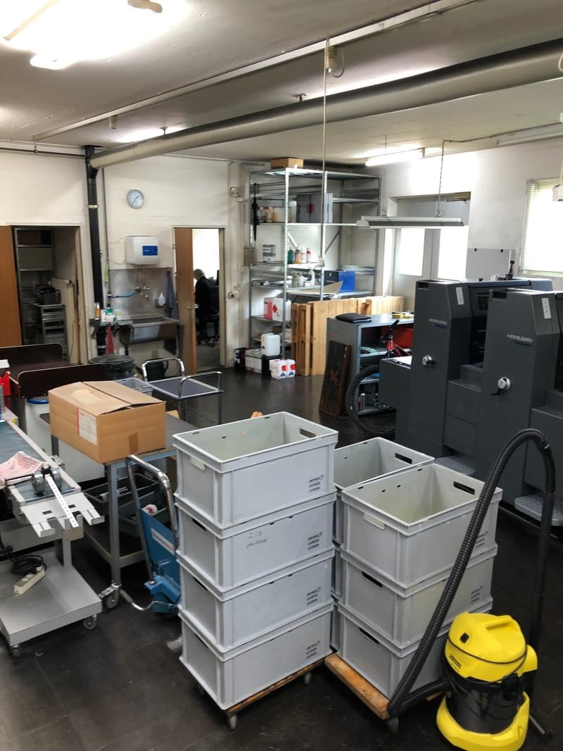 Storage area with several plastic bins, a cart, shelves, boxes, and printing equipment.