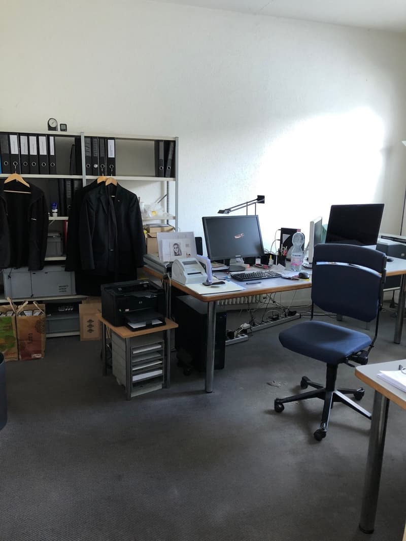 An office with a desk, chair, computer, printer, shelves with storage boxes, papers and bags.