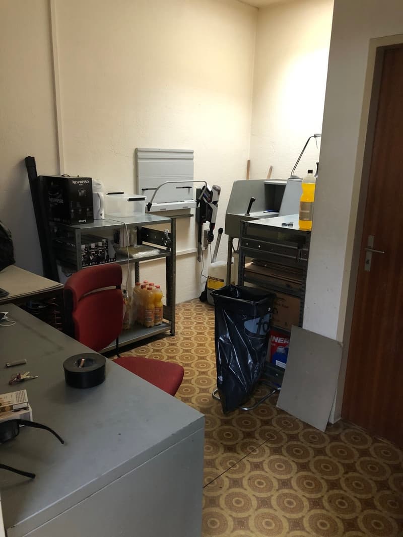 office room with red chair, tables, shelves, storage boxes, black trash bin, lamps