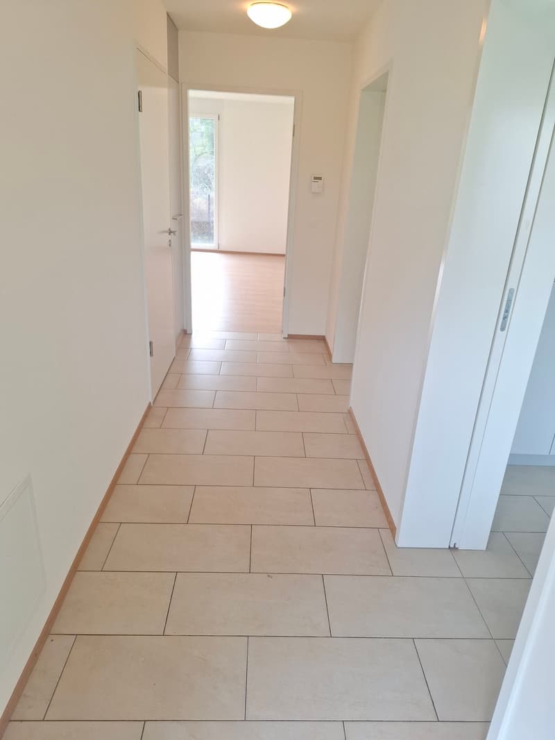 Wide hallway with tiled flooring, white doors, light on ceiling