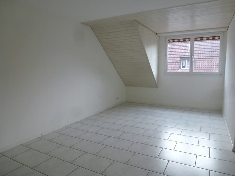 Empty room with white walls, white tiled floor, single window, slanted roof