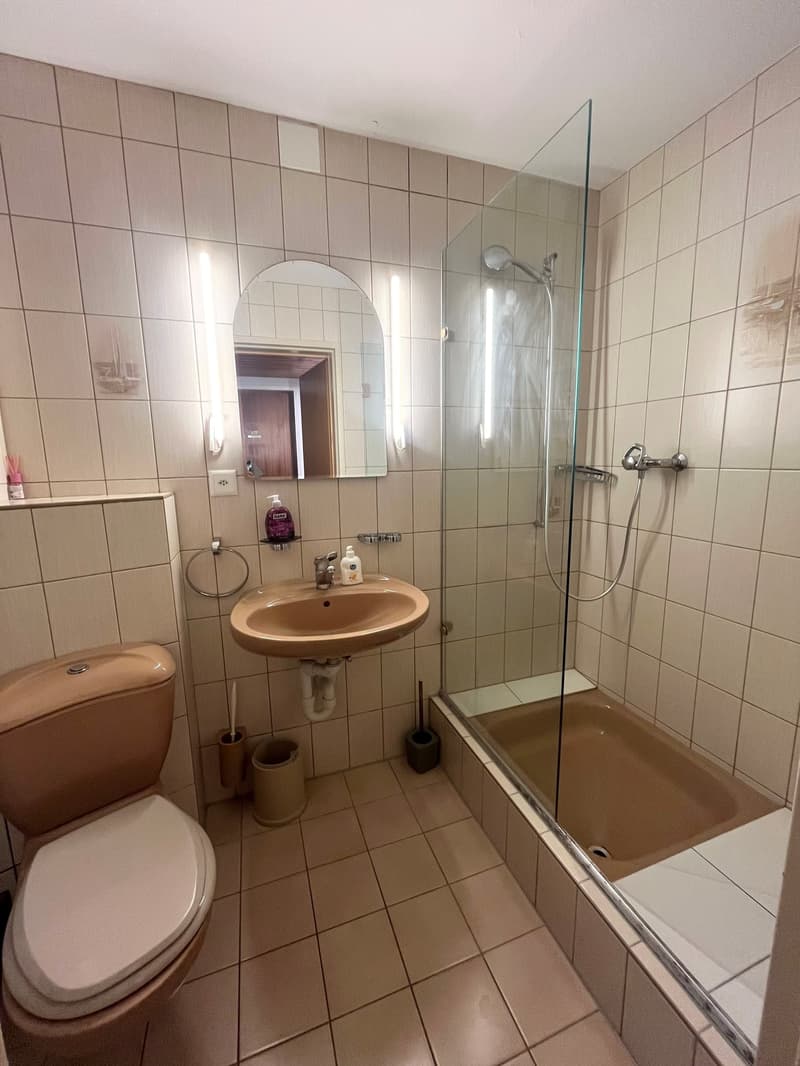 Bathroom with toilet, sink, shower, and mirror. Beige tiles.