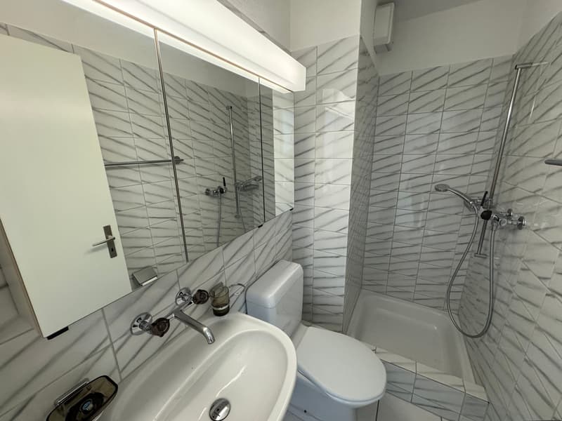 bathroom with white tiles, modern fixtures, shower with glass door, white toilet, sink, large mirror