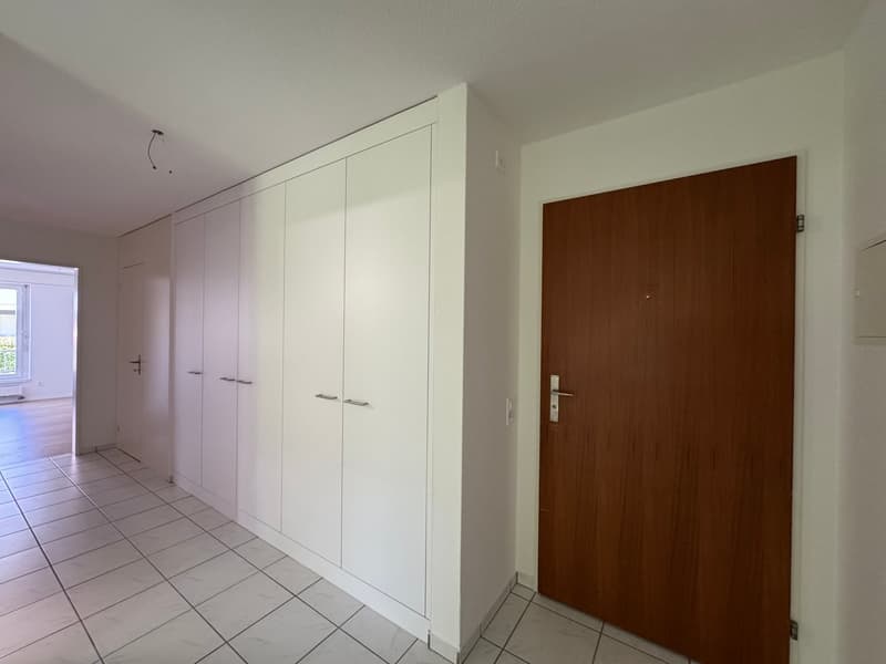 Empty room with white tiled flooring, white walls, a wooden door, built-in closets