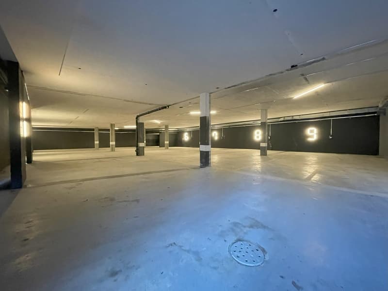 Large indoor parking garage with numbered parking spots, concrete floor, and overhead lighting.
