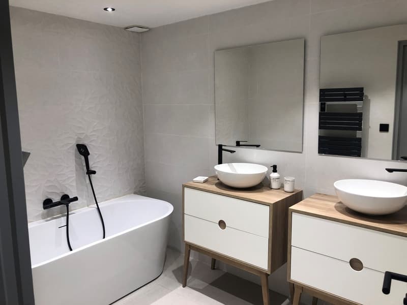 Modern bathroom with bathtub, double sinks, and vanity units. White tiles, black fixtures.