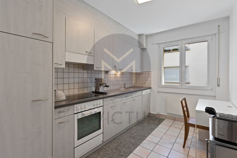 Cuisine habitable / a small kitchen with white cabinets, a stove, sink, and a window