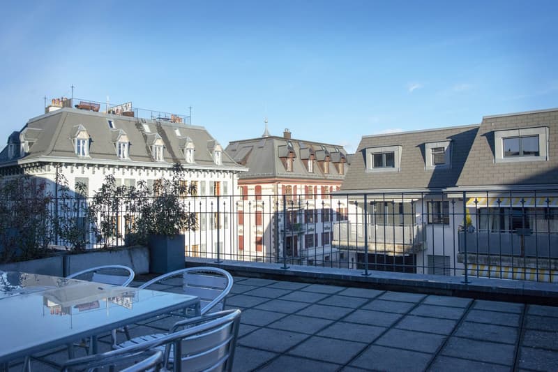 Terrace with tables and chairs, multiple buildings in the background, fence, plants