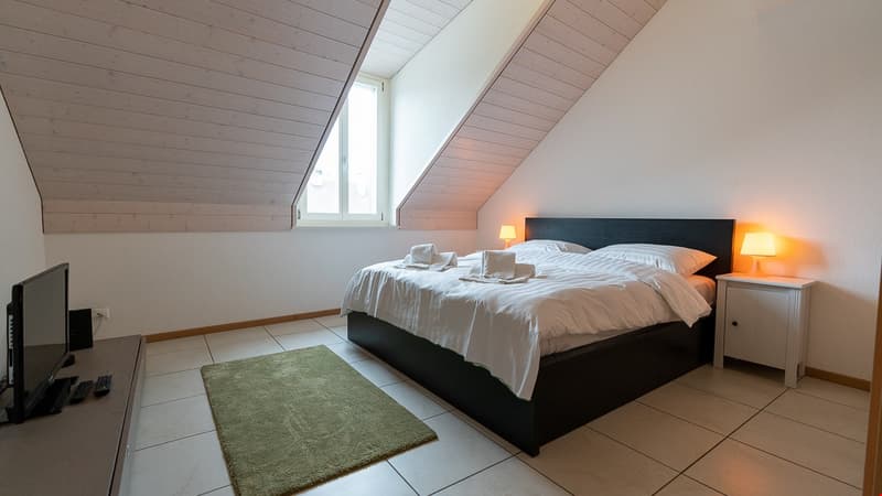 Bedroom with bed, nightstands, lamps, carpet, television, speaker, and a window with daylight.