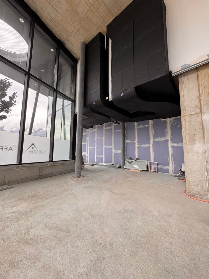 Concrete floor, glass walls, speaker system, exposed brick wall, pipes on the floor, white walls, wooden pole, unfinished walls