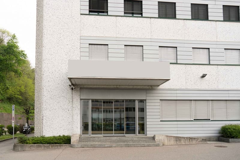 modern building, white exterior, glass entrance, multiple windows, security camera, steps leading to entrance
