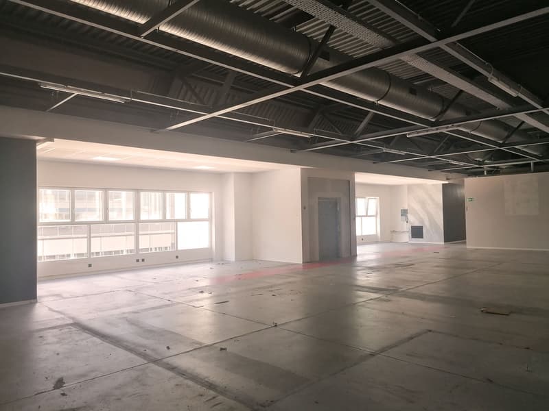 Empty room with large windows, concrete floor, metal beams, and exposed pipes
